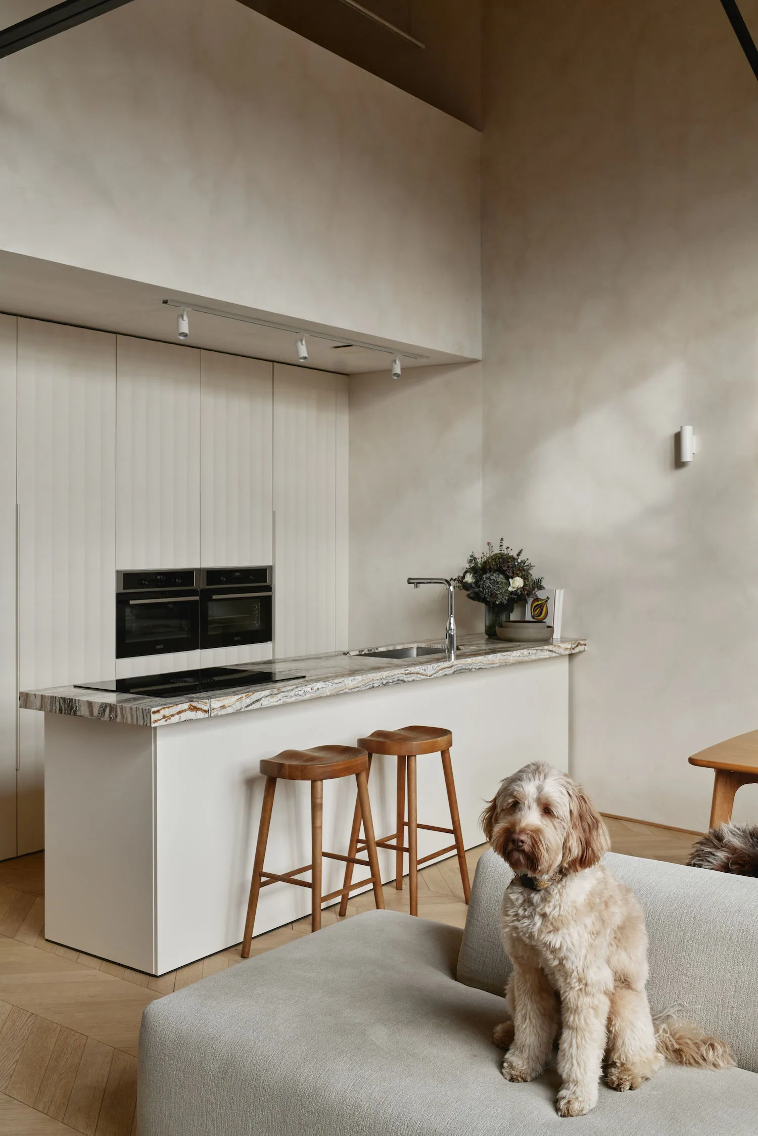 A modern residential kitchen featuring white cabinets, a marble countertop, and two wooden stools.