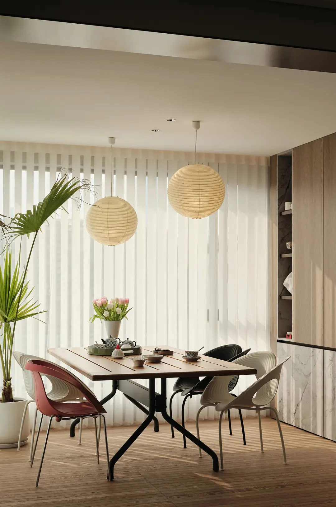 Modern dining room featuring a wooden dining table and chairs, with a potted plant and a vase of flowers on the table, and pa