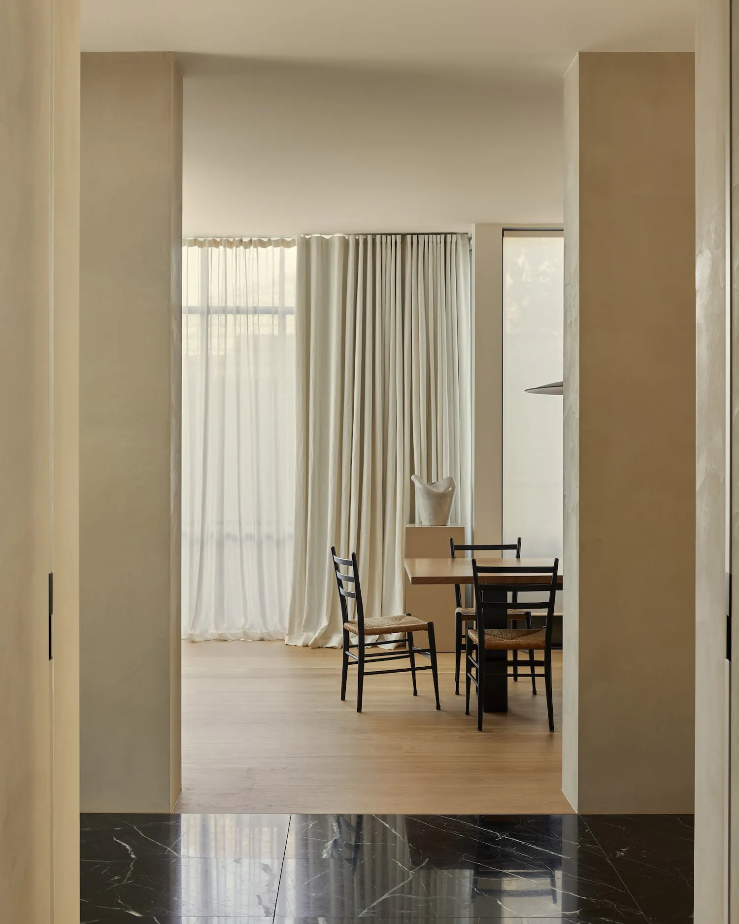 Minimalist dining room with wooden table and chairs, featuring sheer curtains and natural light.