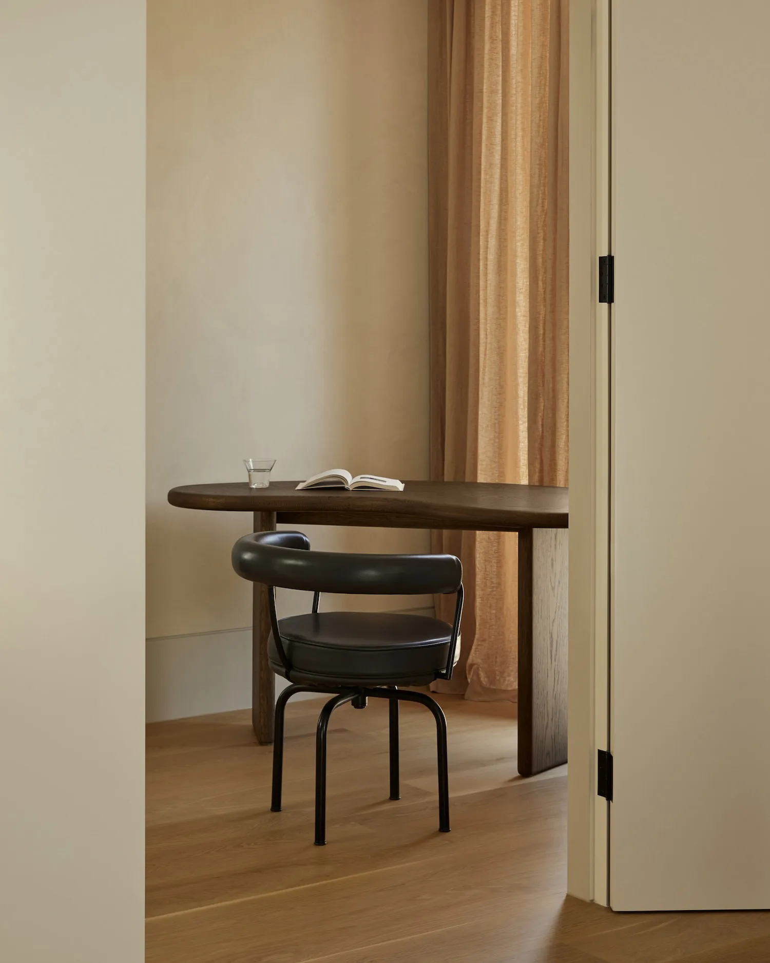 A minimalist home office featuring a wooden table with a glass of water and an open book, accompanied by a comfortable black