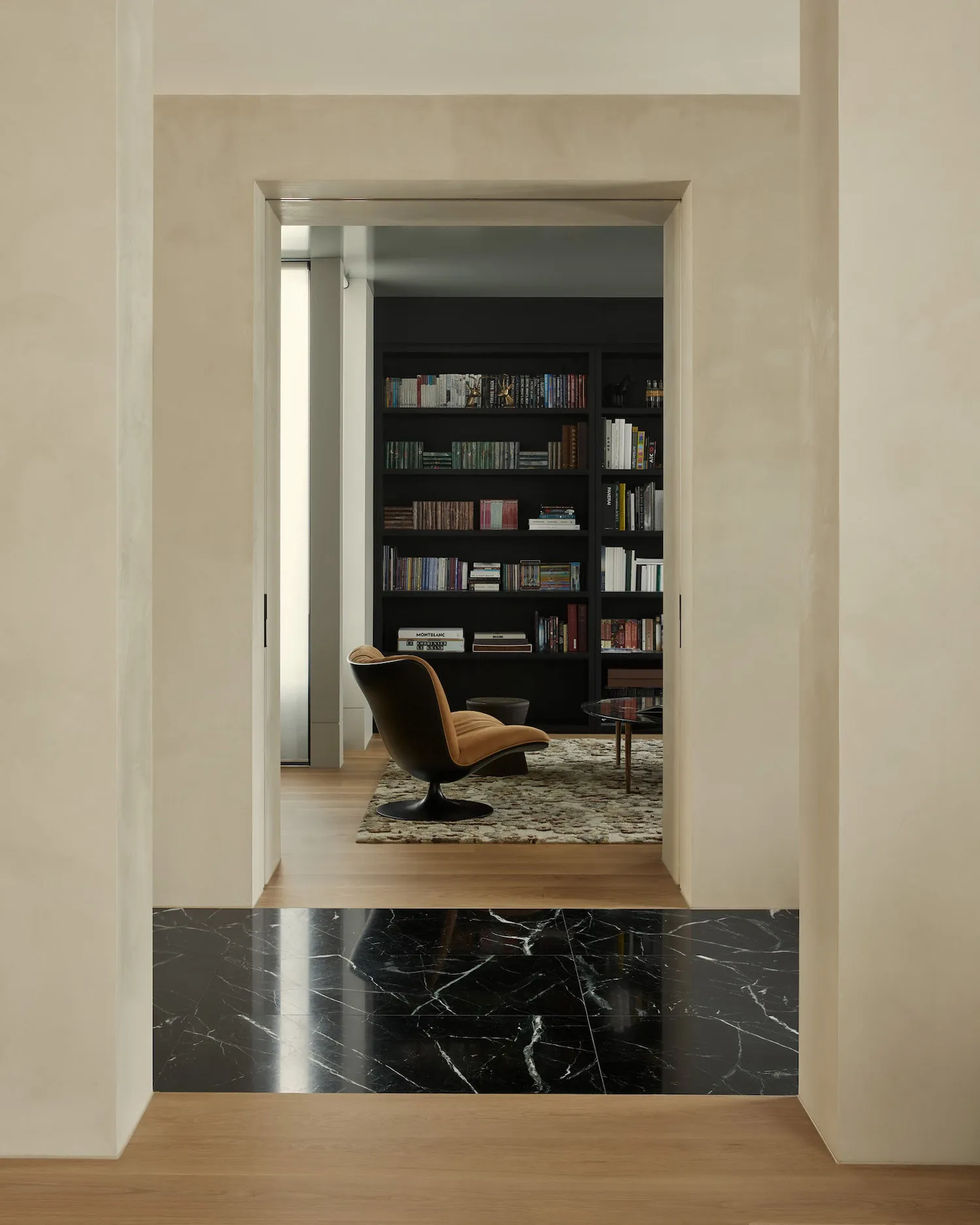 Modern living room featuring wood and marble flooring, dark bookshelf, and a cozy reading nook with a comfortable chair and r
