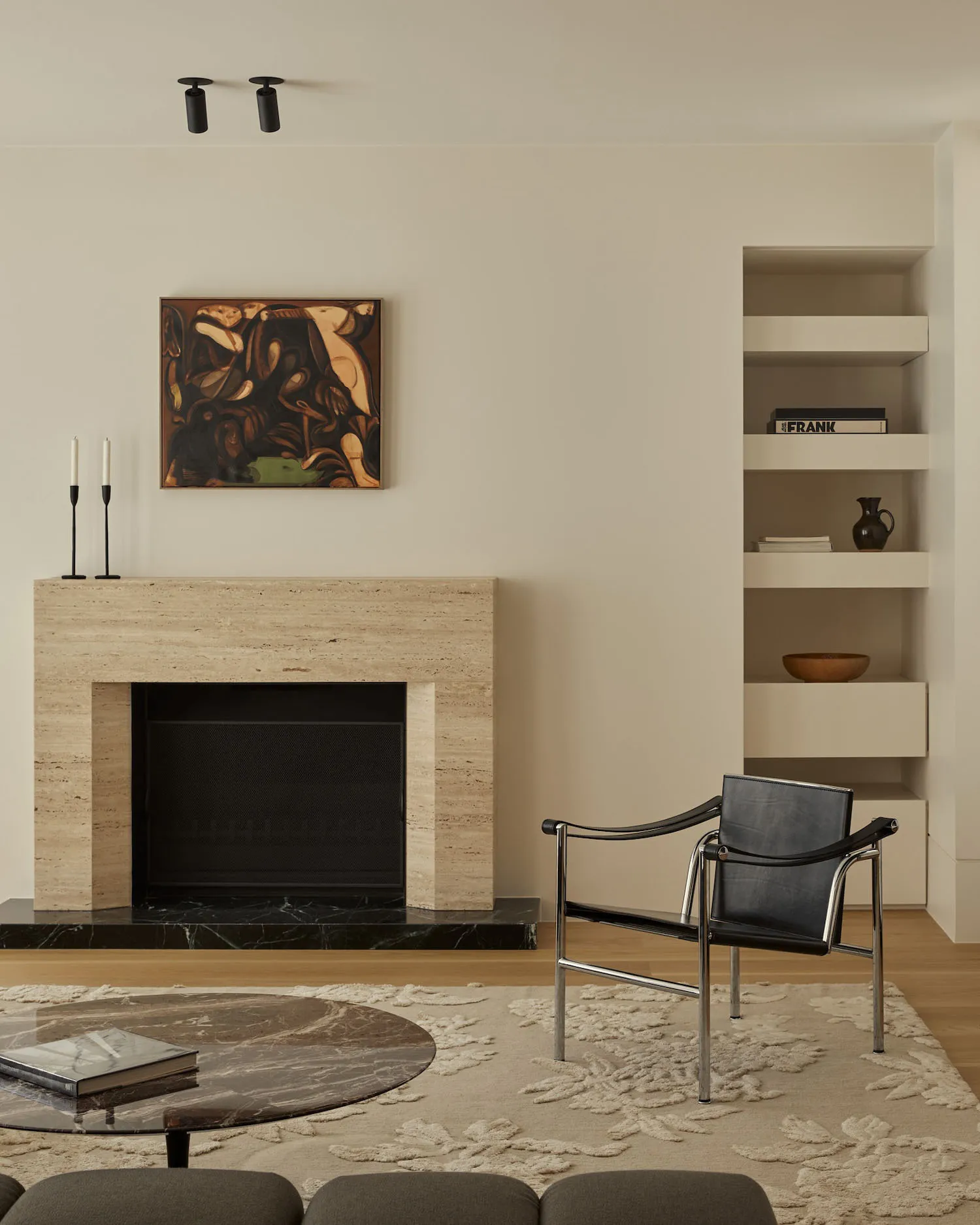 A minimalist living room features a marble fireplace and coffee table, a black leather armchair, and a round marble coffee ta