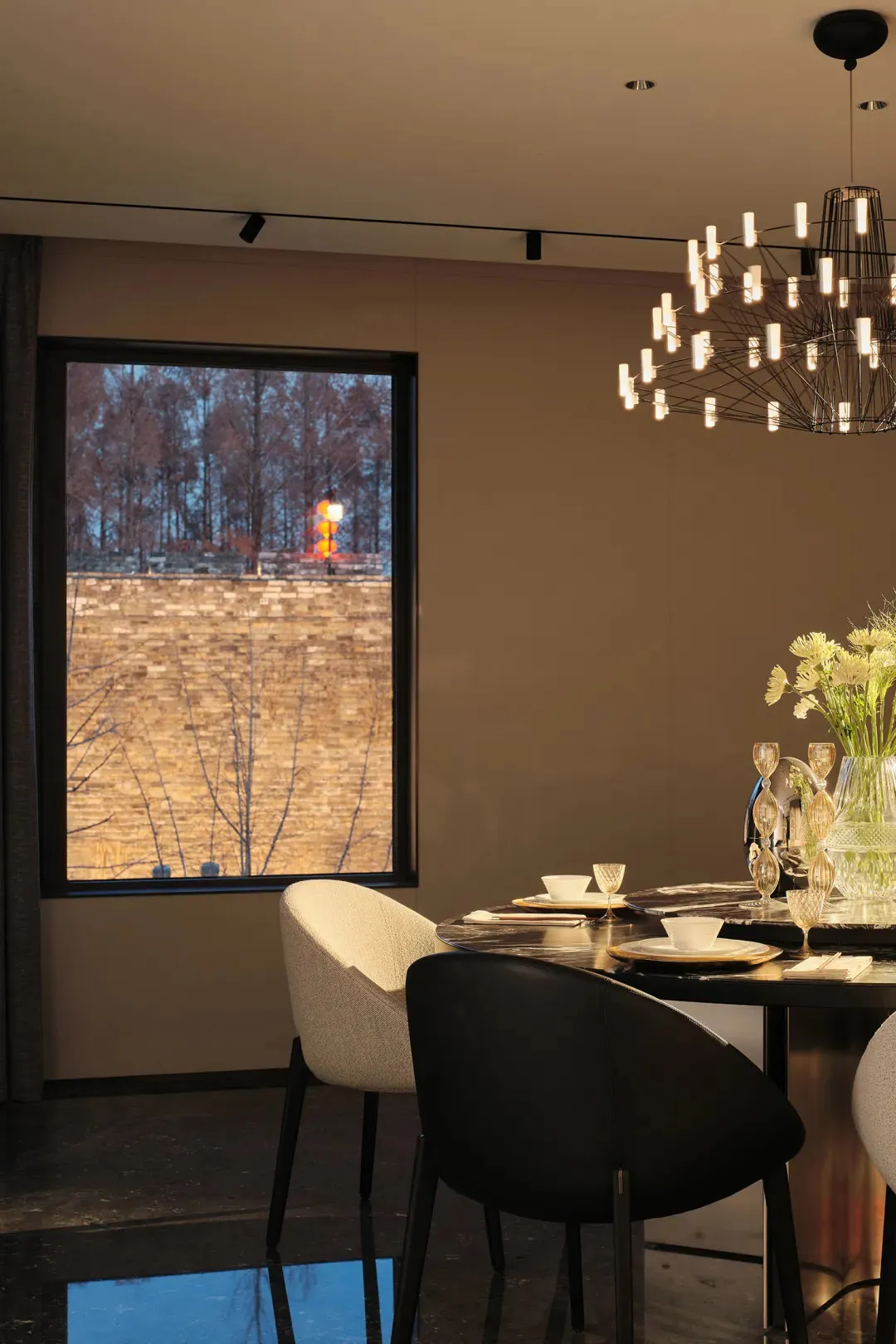 A modern dining room featuring minimalist furniture, a round table with a minimalist chandelier, and a large window overlooki