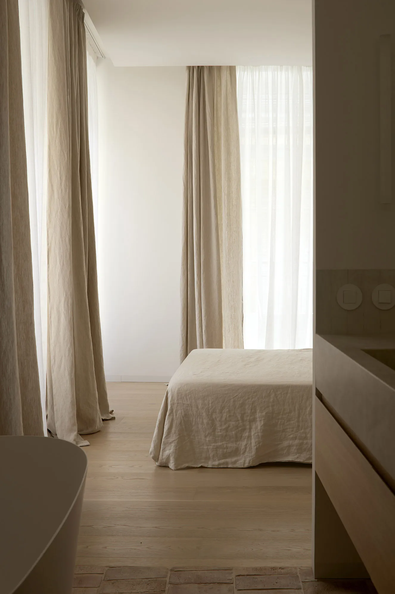 A minimalist bedroom with neutral-toned curtains, a single bed, and wooden flooring.