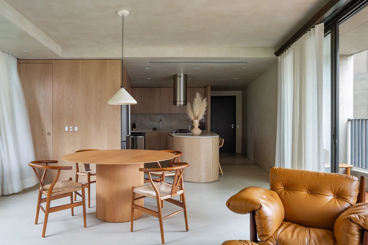 A modern, minimalist residential kitchen with a round dining table and wooden furniture.