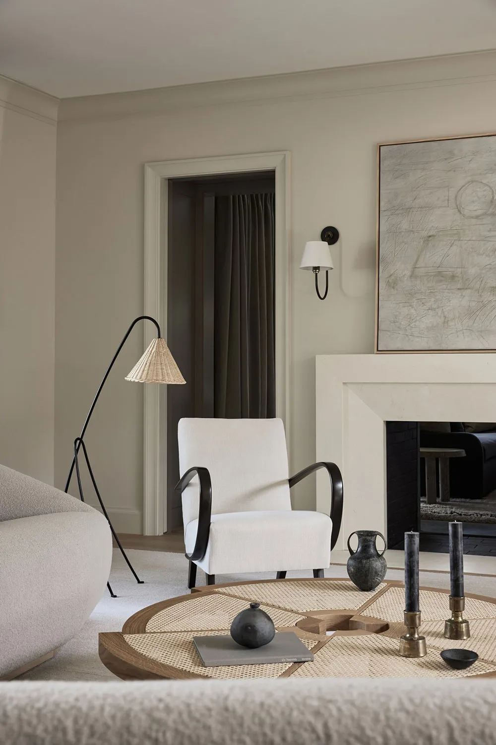 A minimalist living room with a taupe accent wall, a white armchair, and a rattan and wood coffee table.