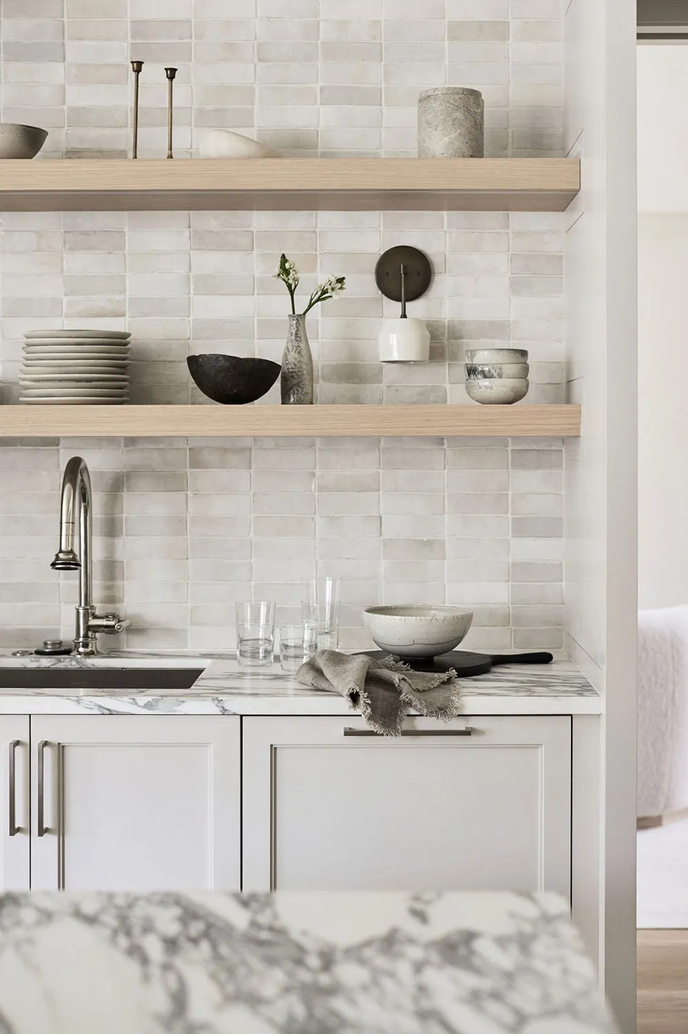 Minimalist kitchen with white cabinets, wooden shelves, ceramic tiles, and marble countertop.