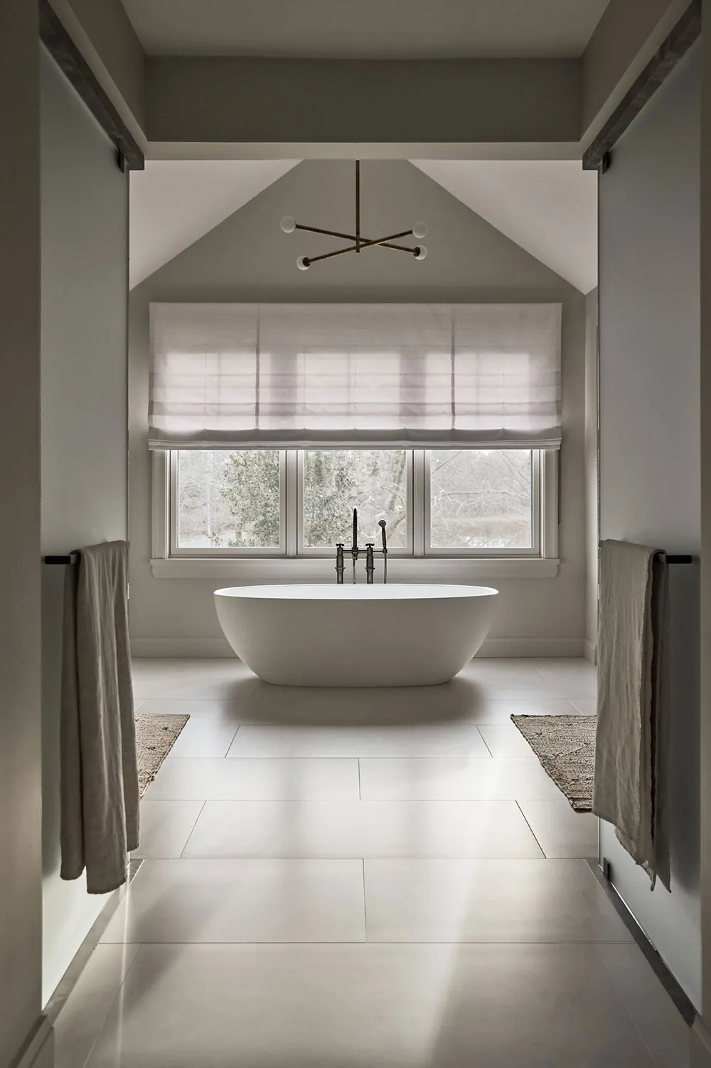 Modern bathroom with a white oval-shaped bathtub, floor-to-ceiling windows, and gray tile flooring.