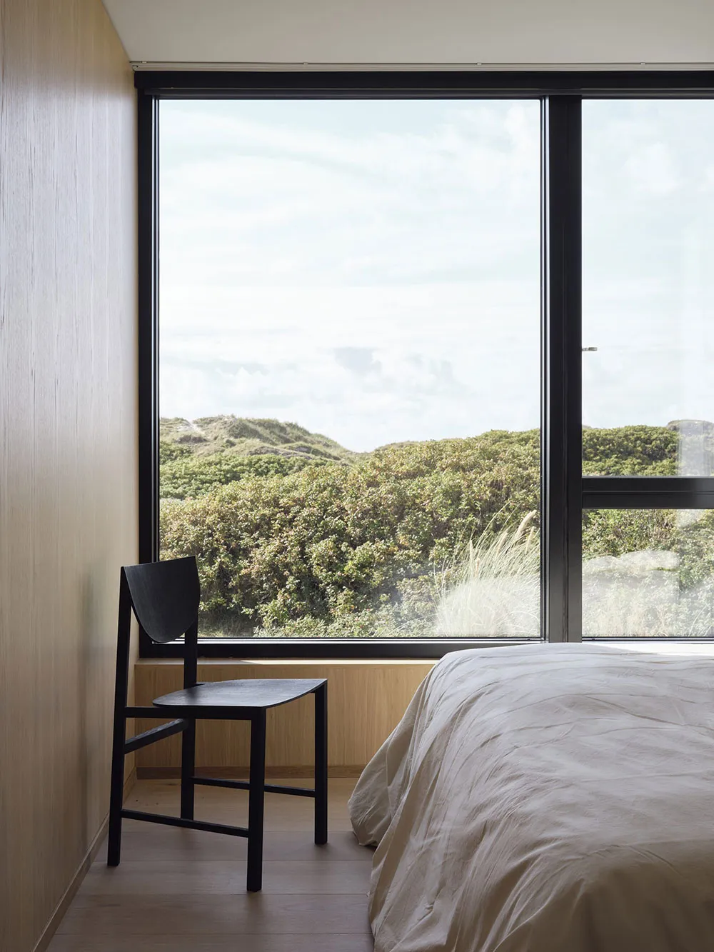 A minimalist bedroom with a large window overlooking greenery.