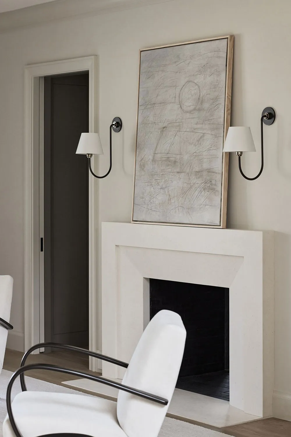 A minimalist living room with a concrete fireplace, abstract artwork, and white furniture.