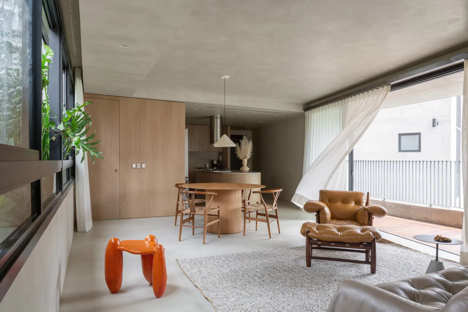 A modern residential space featuring a concrete interior with a round dining table, wooden chairs, and a large window allowin