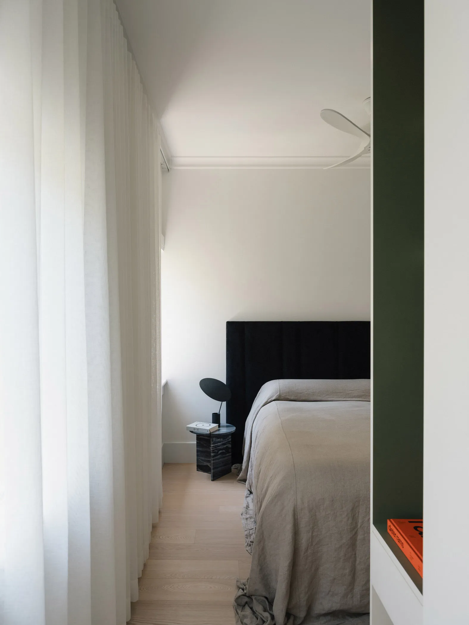 A minimalist bedroom featuring neutral fabrics and a large window with sheer curtains.