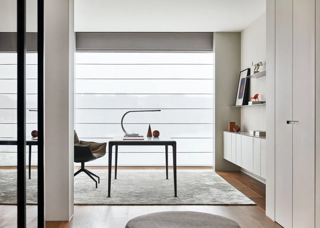 A minimalist home office featuring a black metal table with a lamp, books, and decorative objects.
