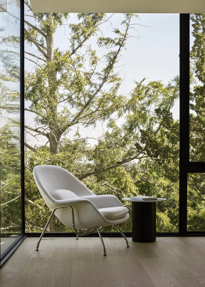 A minimalist living room with a white upholstered armchair, black metal side table, and wooden flooring, featuring a view of