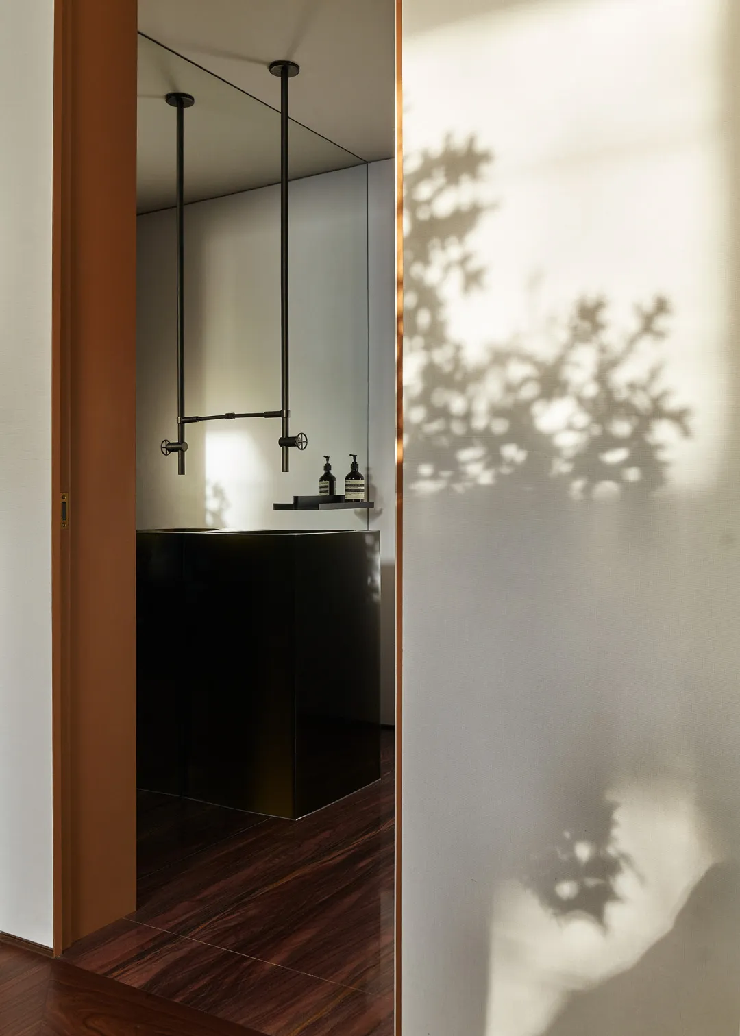 Modern bathroom interior with walnut flooring and steel fixtures, showcasing sleek design with natural light and shadows from