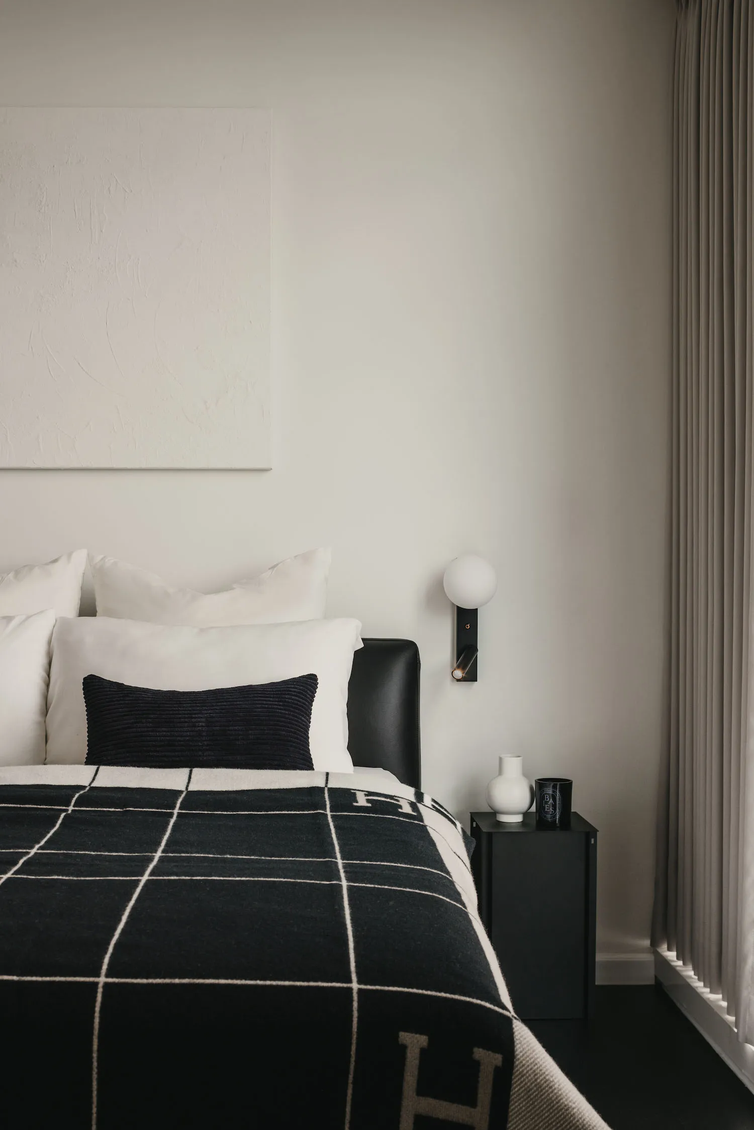 A minimalist bedroom featuring a black and white checkered blanket, a white pillow, and a leather bedframe.