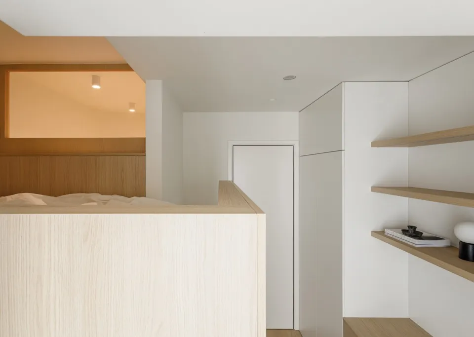 A minimalist residential interior with white walls, wood accents, and a floating shelf.