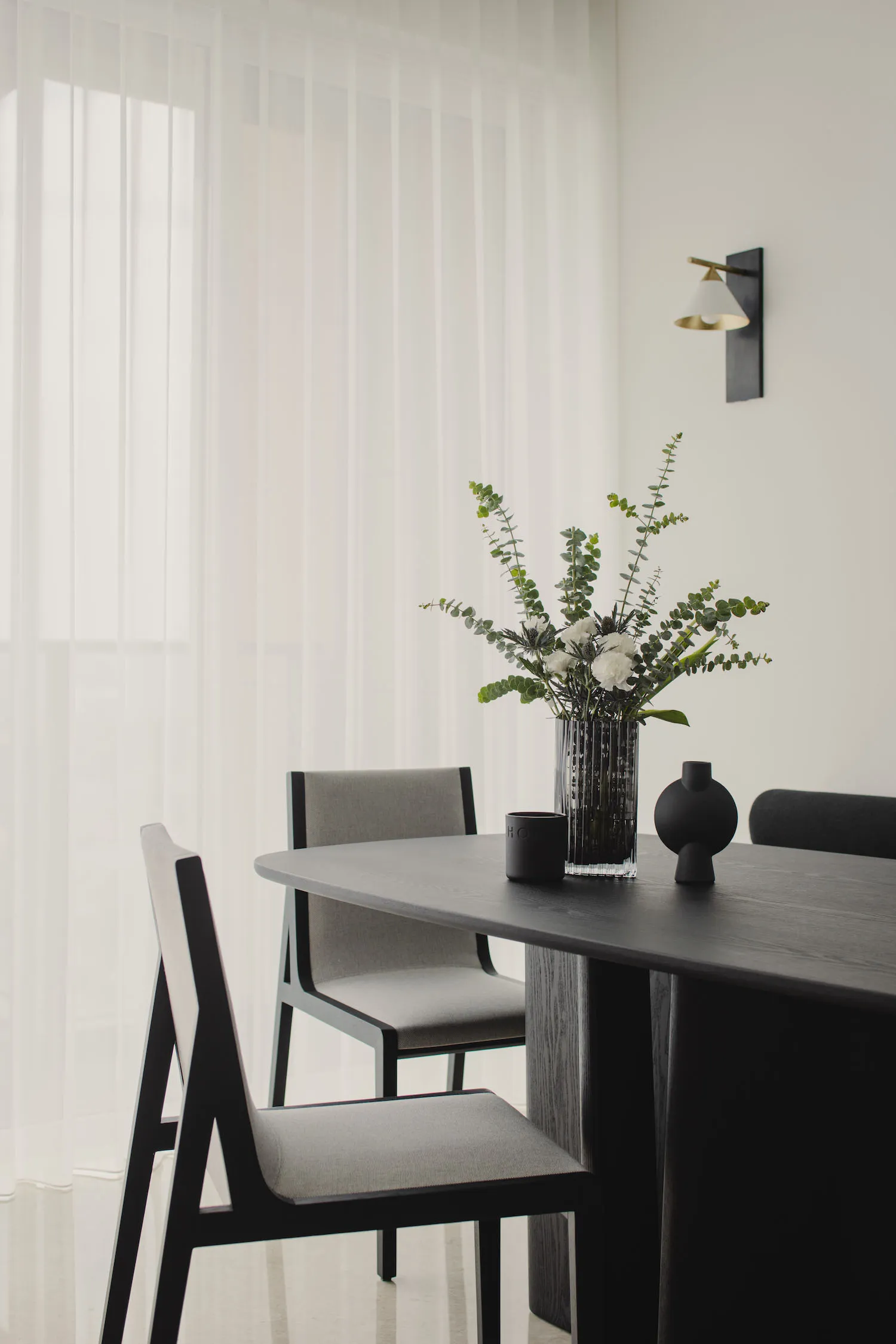 A modern dining room with wooden furniture, including chairs and a table, adorned with a vase of flowers and decorative objec
