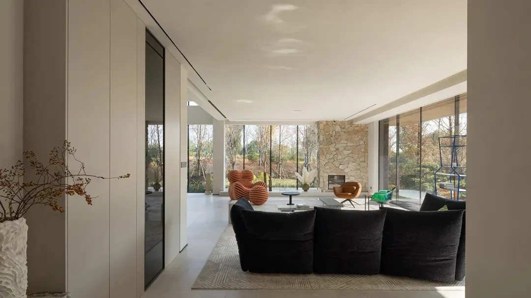 Modern living room with glass walls, stone fireplace, and wooden furniture.
