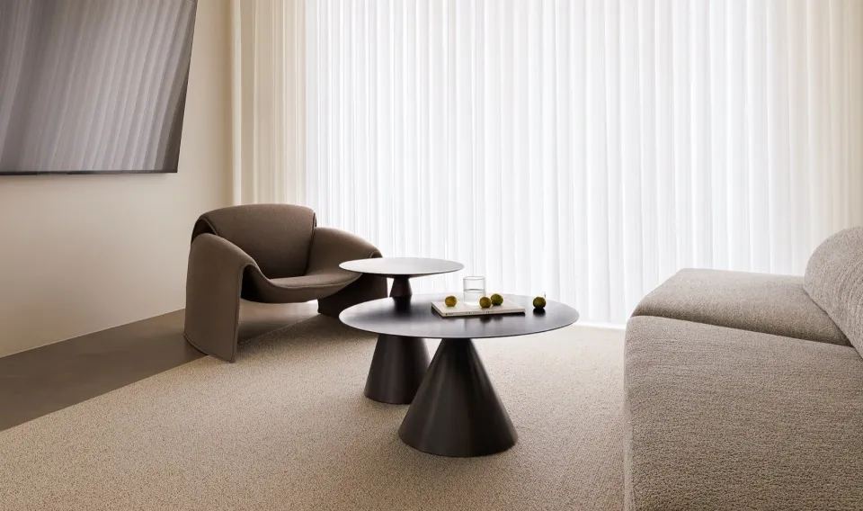A modern living room with textured fabric furniture, a coffee table with a book and decorative objects, and a large window wi