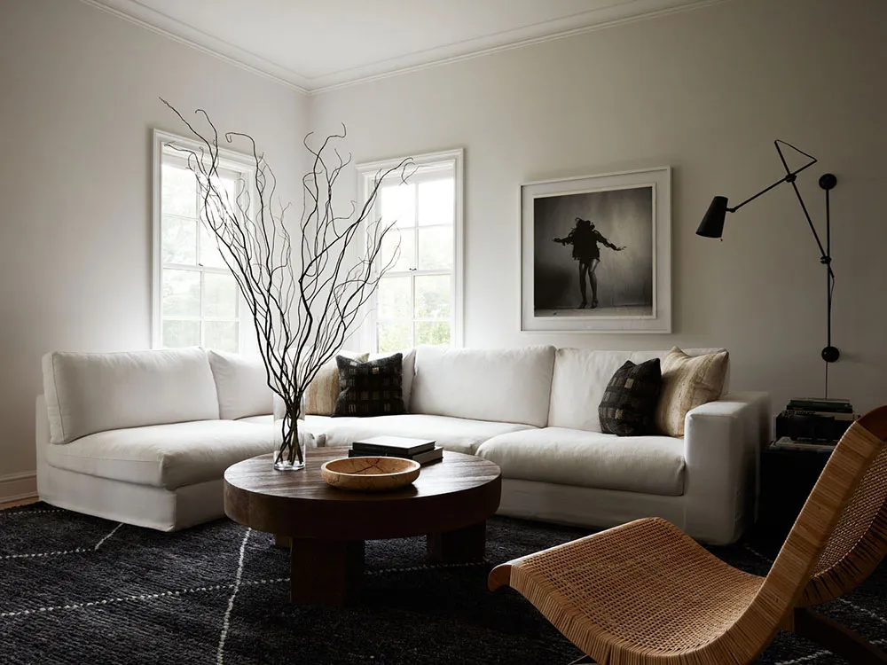 A modern minimalist living room with a white sectional sofa, wooden coffee table, and black and white photograph on the wall.