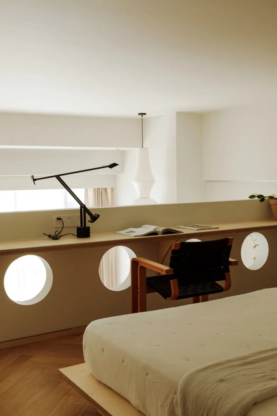 A minimalist bedroom featuring a simple bed with a wooden frame, a black leather armchair, and a floating desk with a black l