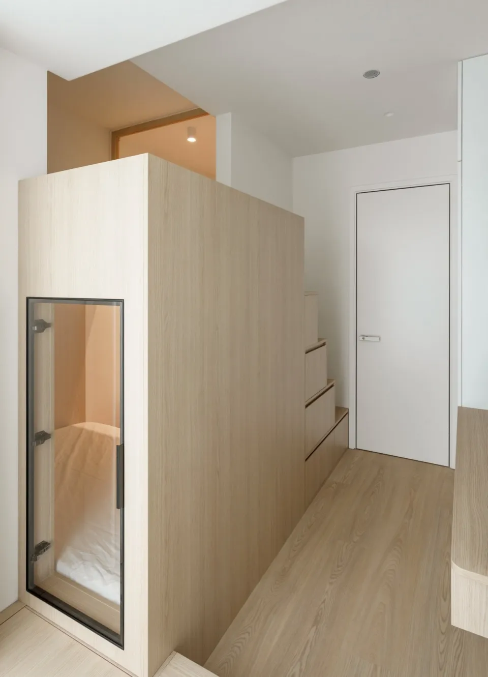 A minimalist interior design featuring a white door, wooden walls, and a glass panel.