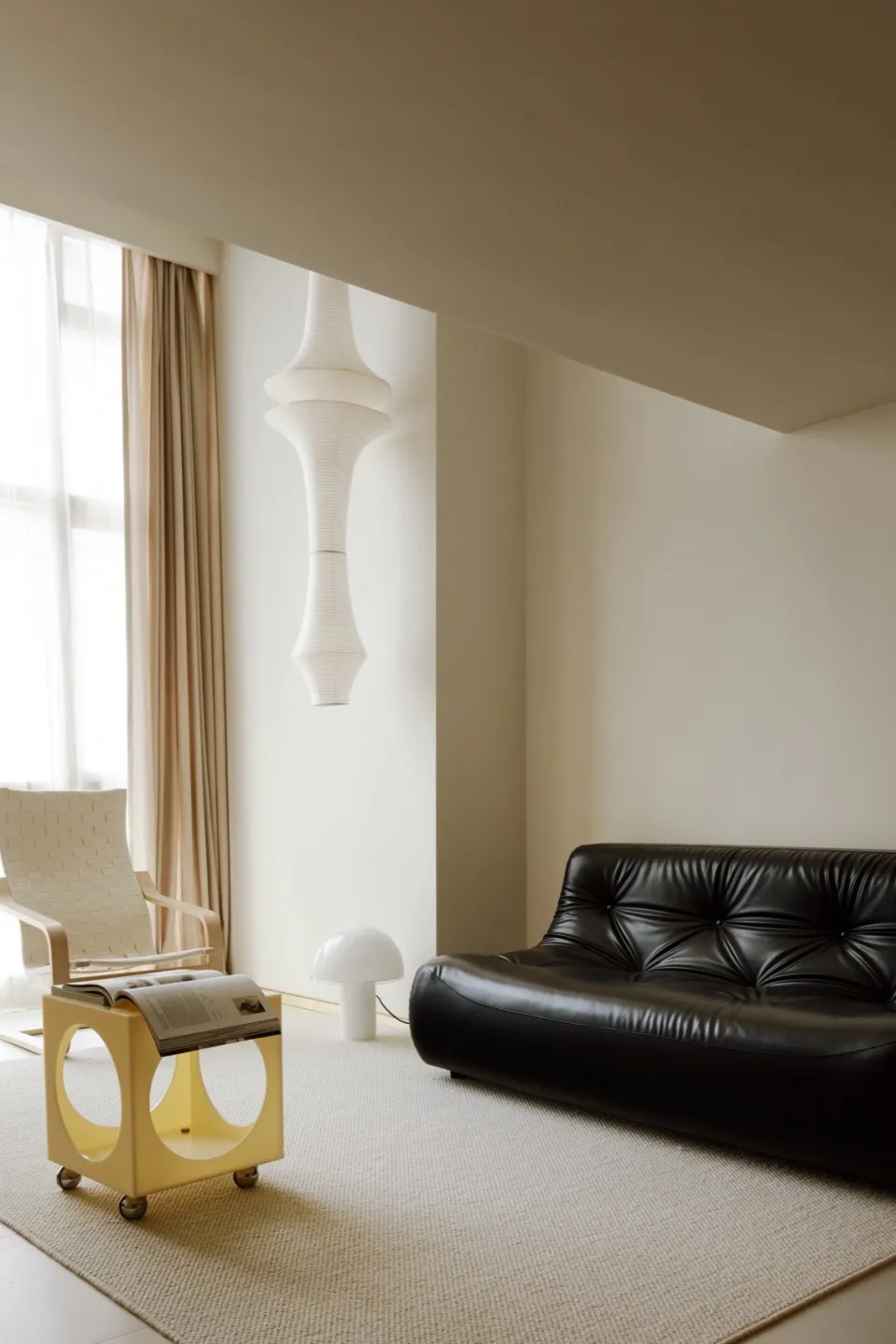 A minimalist living room features a sleek, black leather sofa and a vibrant yellow end table with wheels, set against a backg
