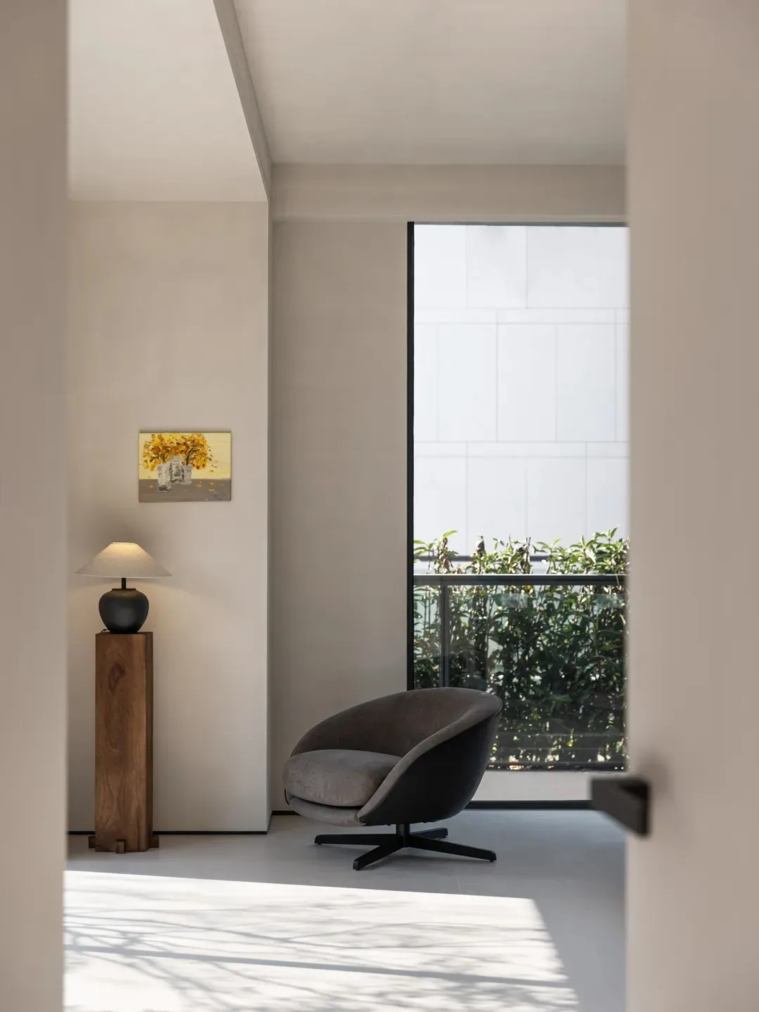 A modern living room featuring a minimalist armchair, a small wooden side table with a lamp, and a framed picture on the wall