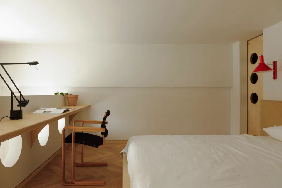 A minimalist bedroom with a wooden bed, desk, and chair
