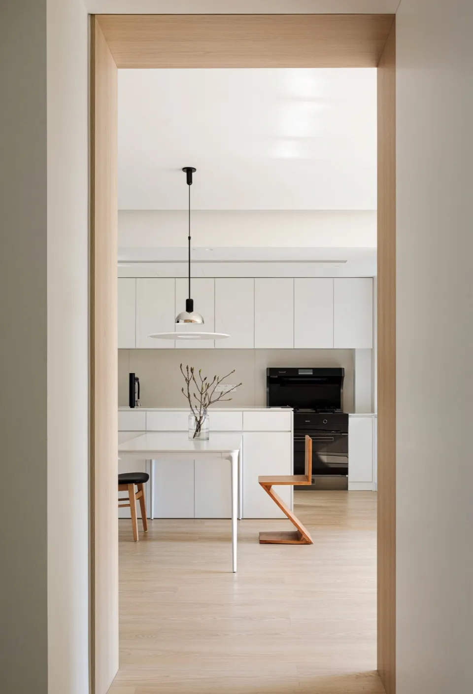A modern kitchen with white minimalist cabinets and wooden flooring.