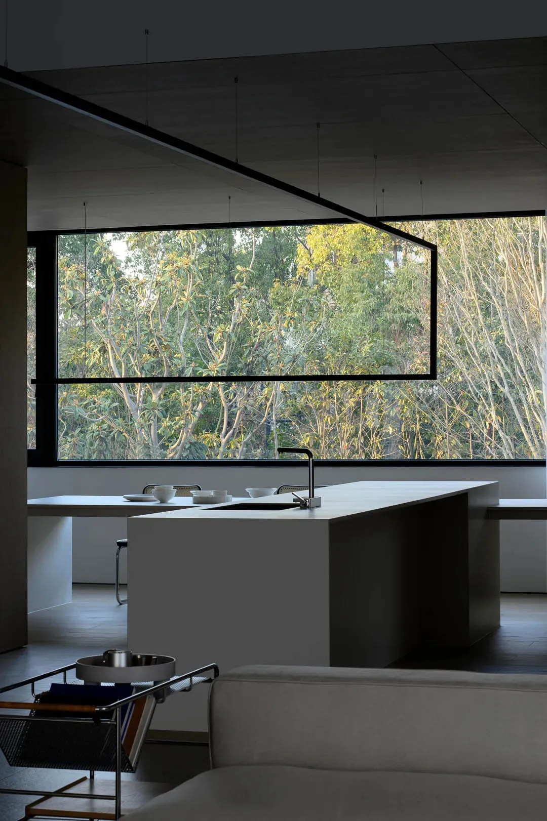 Modern kitchen interior with concrete island and large windows overlooking greenery.