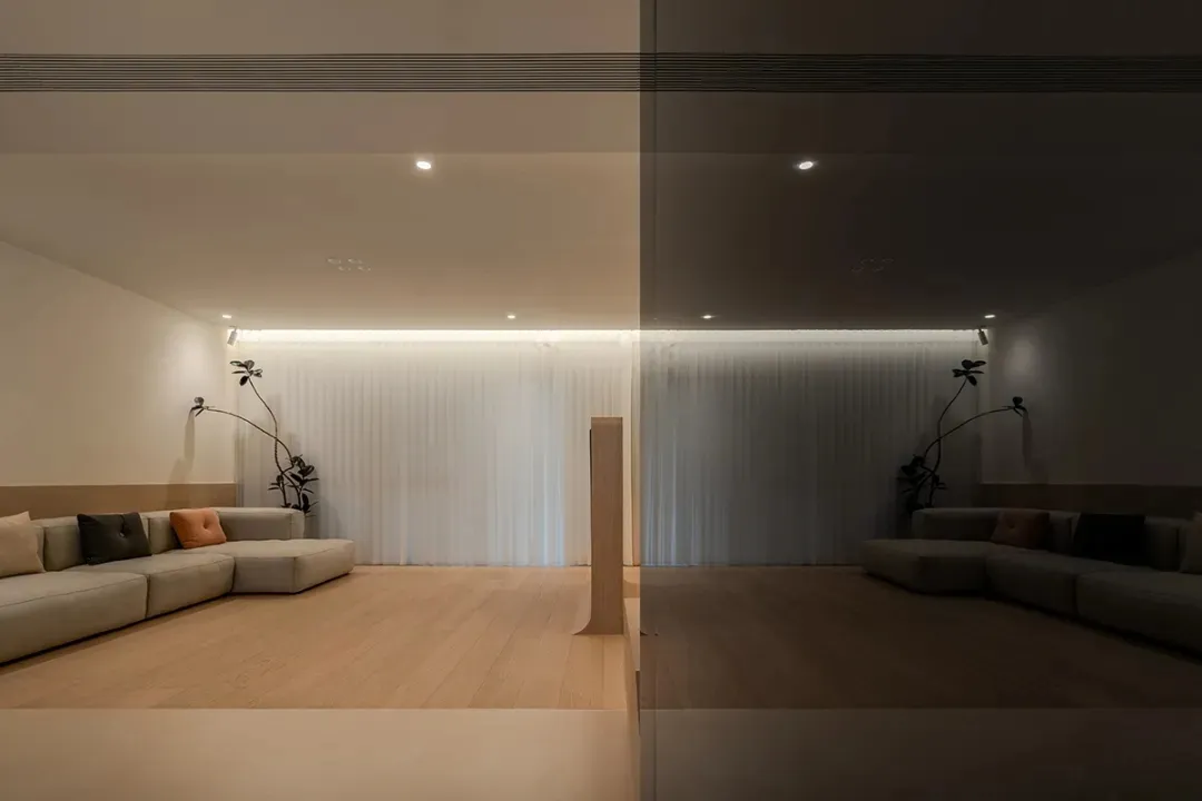 Interior design featuring a modern minimalist living room with light wooden flooring, a sleek glass partition, and a comforta