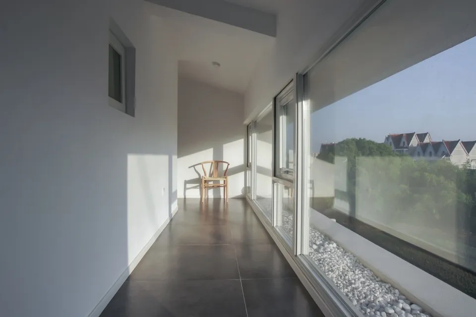 A minimalist residential interior featuring large glass windows with views of greenery.