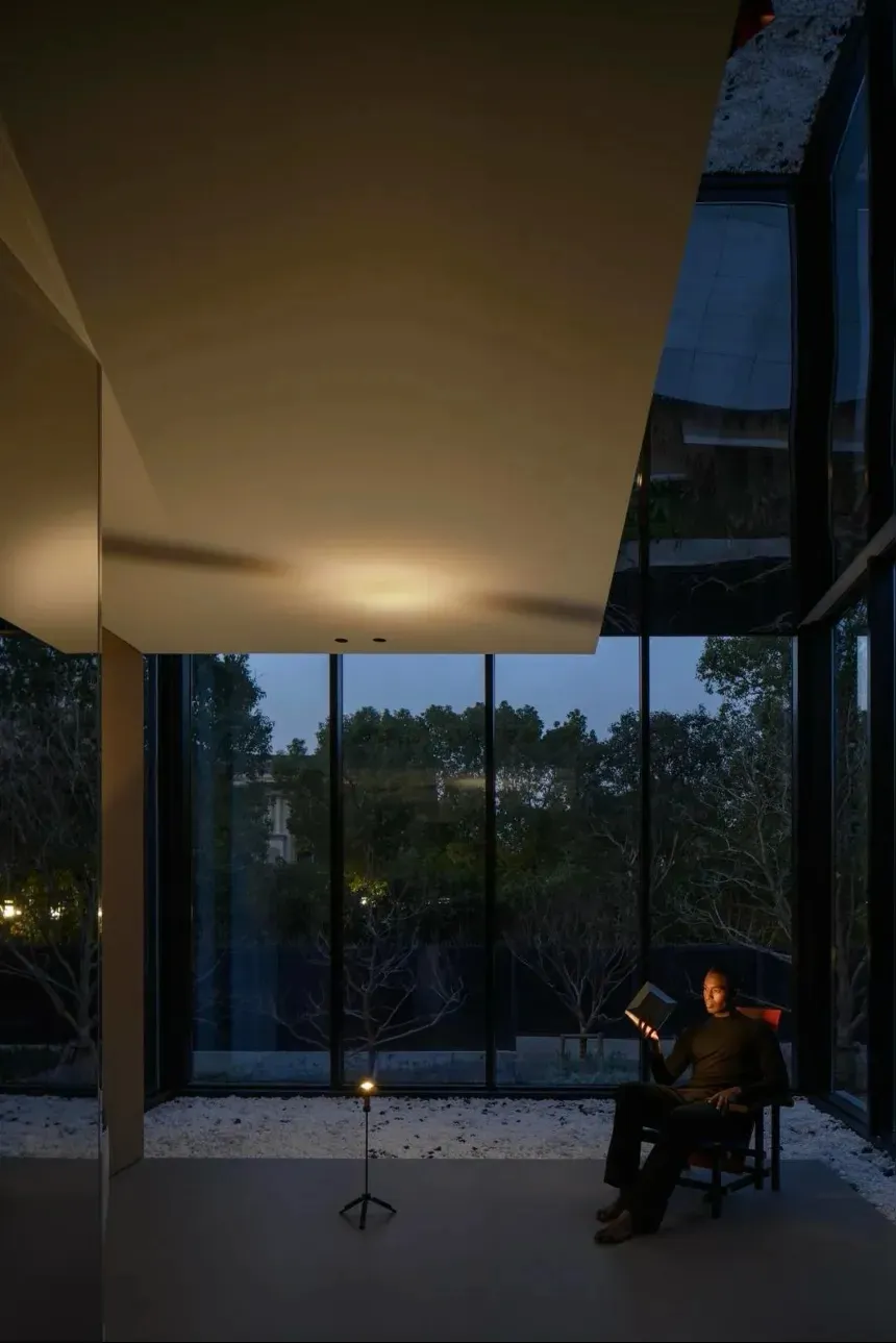 A modern interior design featuring a glass window with a person reading a book at dusk.
