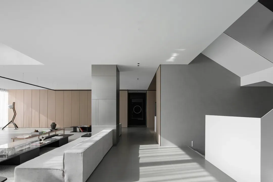 A modern, minimalist living room with concrete flooring and walls, featuring a large white sofa and a low glass coffee table.