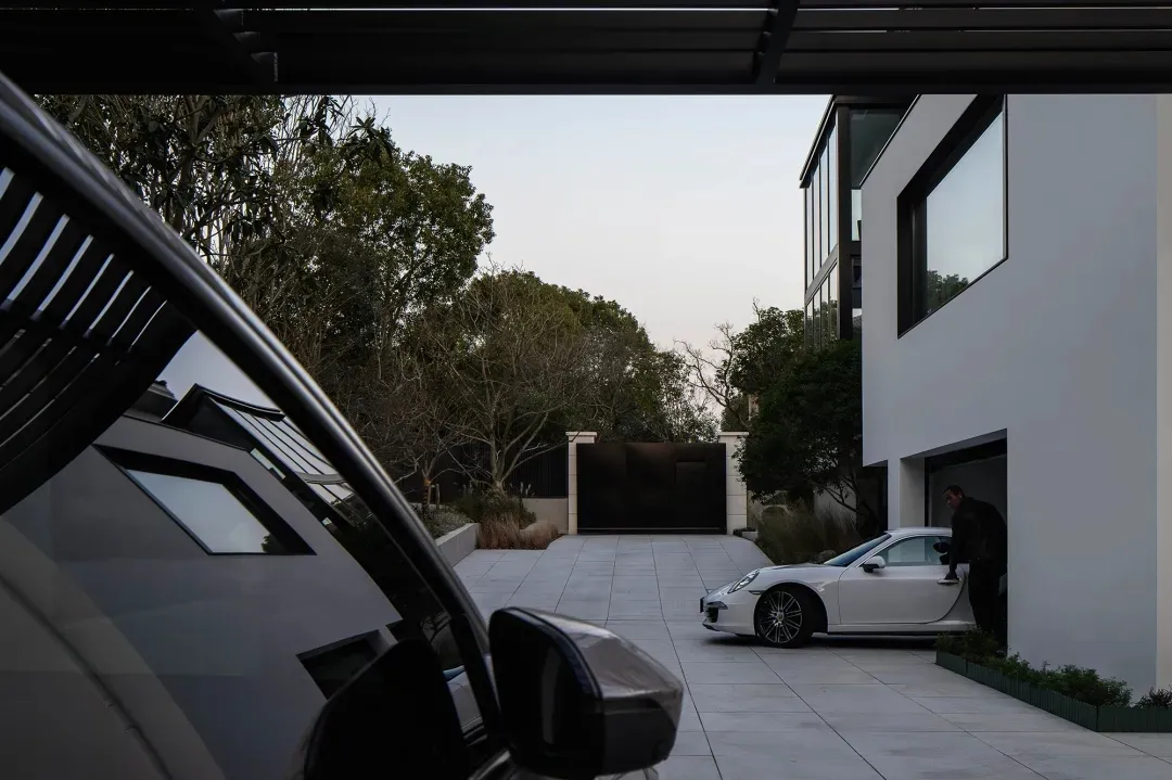 A modern garage with a white sports car parked inside. The exterior features large windows and doors, and the surrounding are