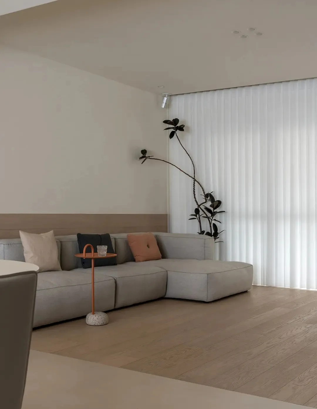 A minimalistic living room with neutral-colored furniture and a large window with vertical blinds.