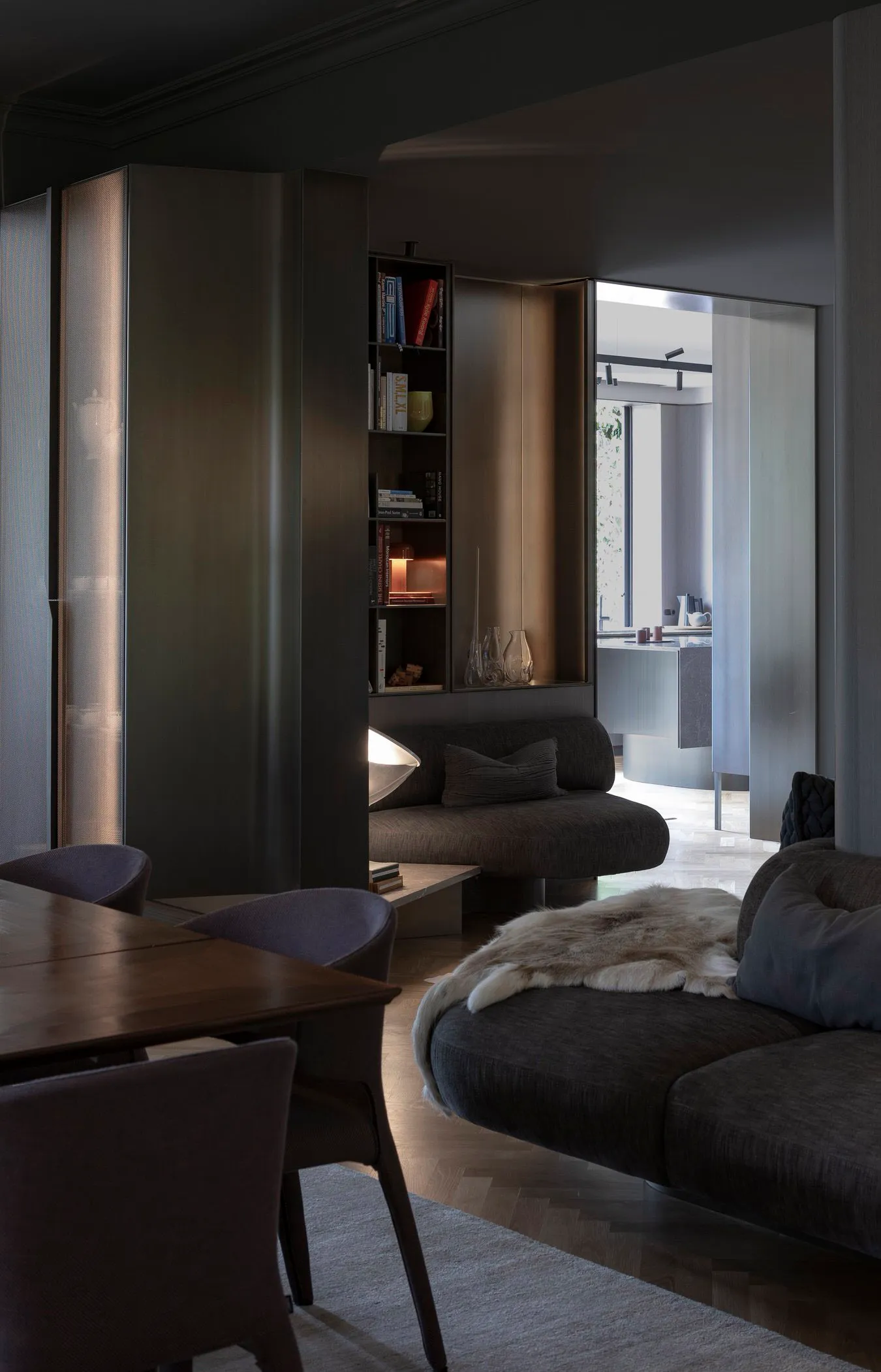 A modern minimalist living room with dark furniture, a bookshelf, and a round sofa with a fur throw.
