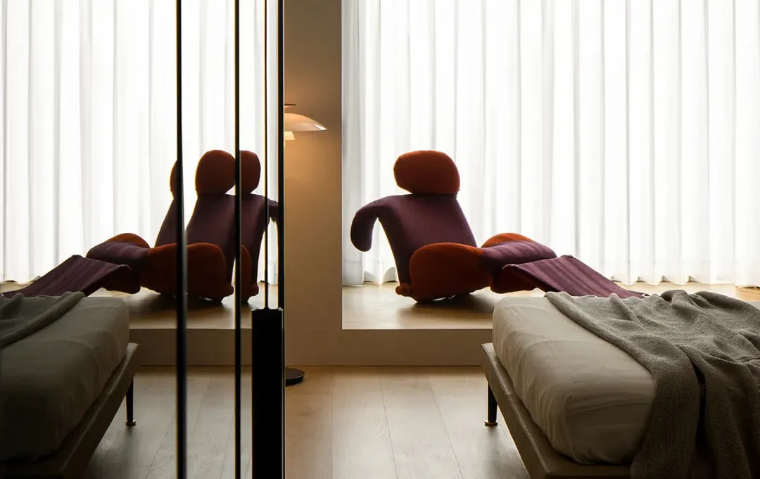 A modern bedroom with minimalist walls, wooden furniture, and upholstered seating.