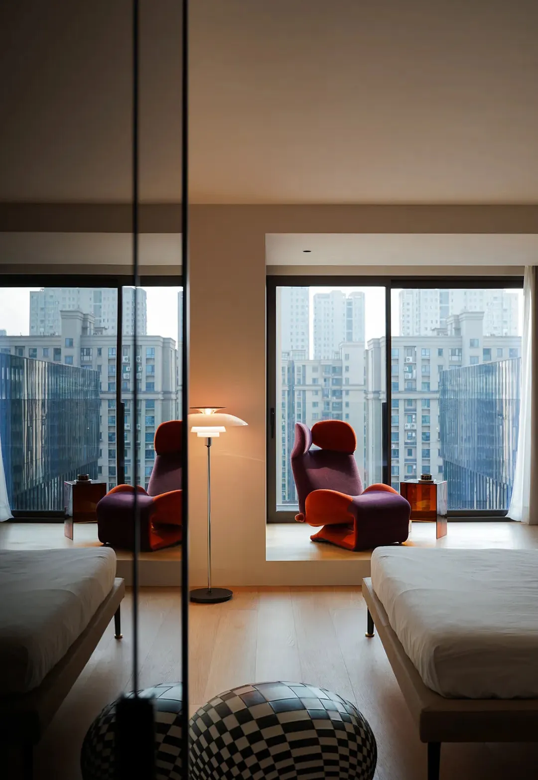 A modern bedroom featuring wooden furniture, white floor, and a large window with a cityscape view.