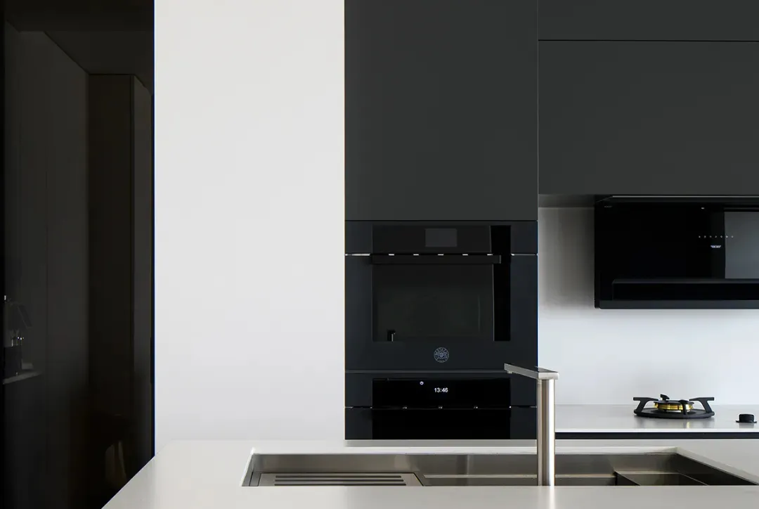 Modern minimalist kitchen with sleek black appliances and white countertops.