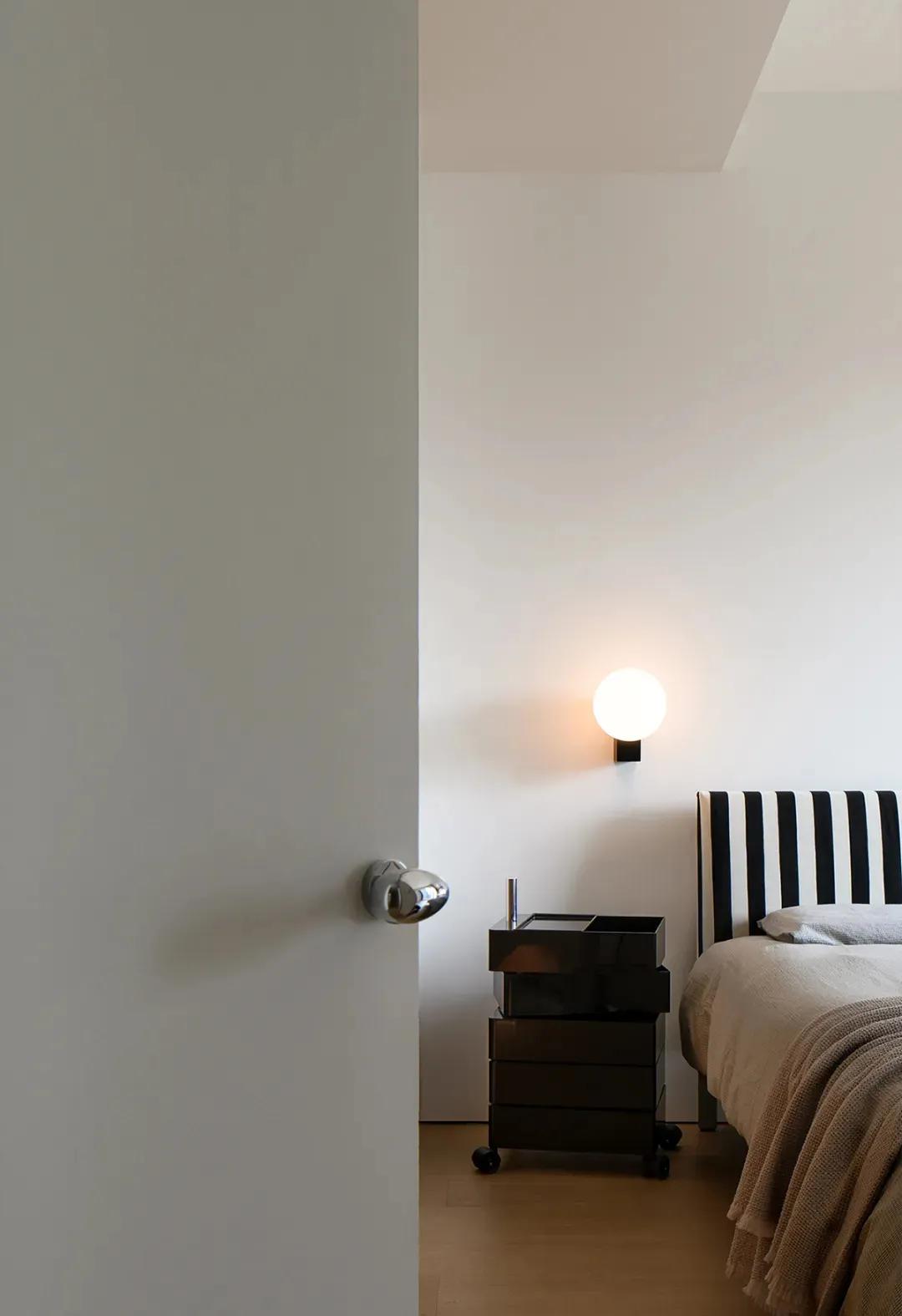 A modern bedroom featuring a black and white striped headboard and a sleek, metallic bedside table with drawers.