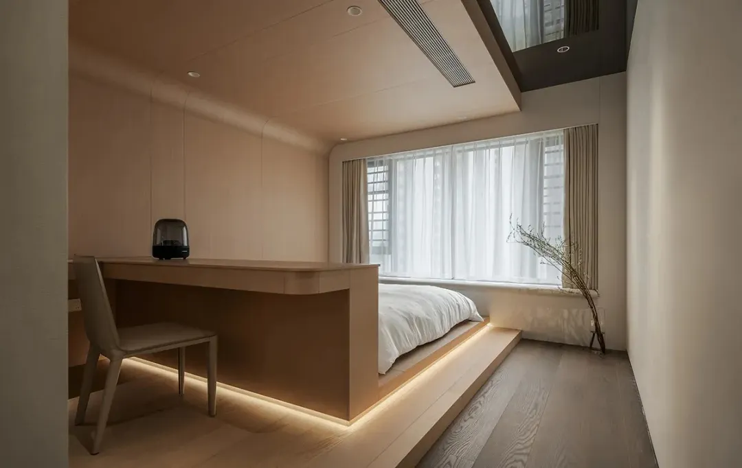 A minimalist bedroom featuring a wooden platform bed and a wooden desk with integrated lighting.