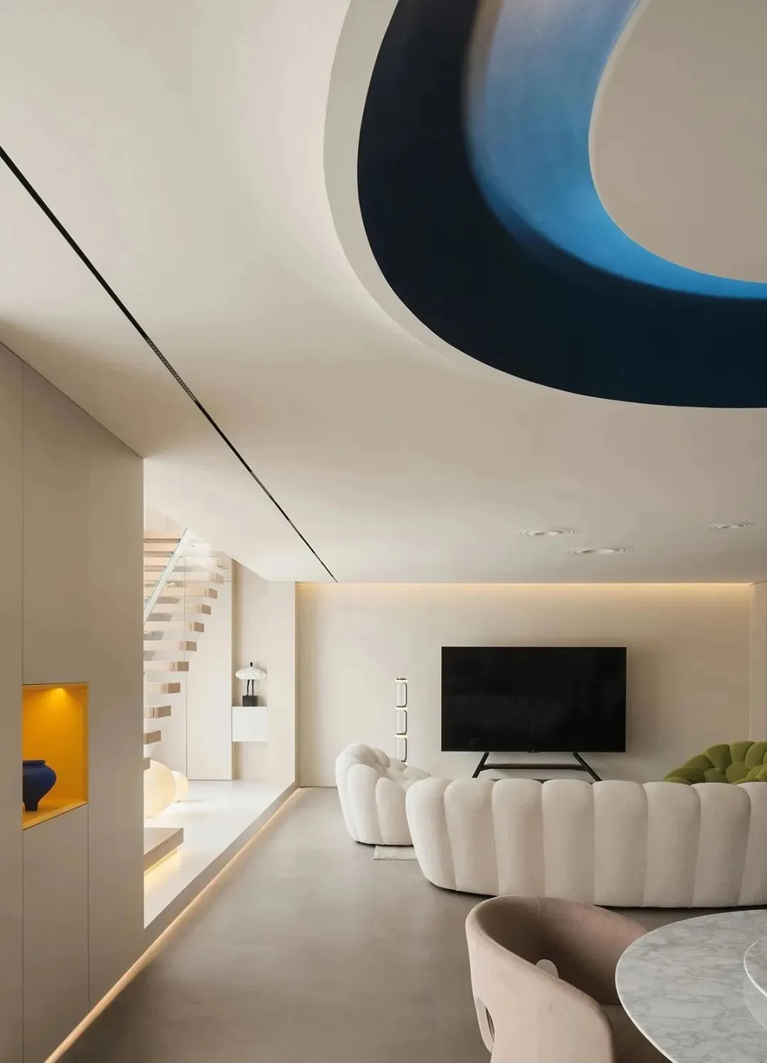 A modern living room with a curvilinear blue ceiling feature and concrete floor.