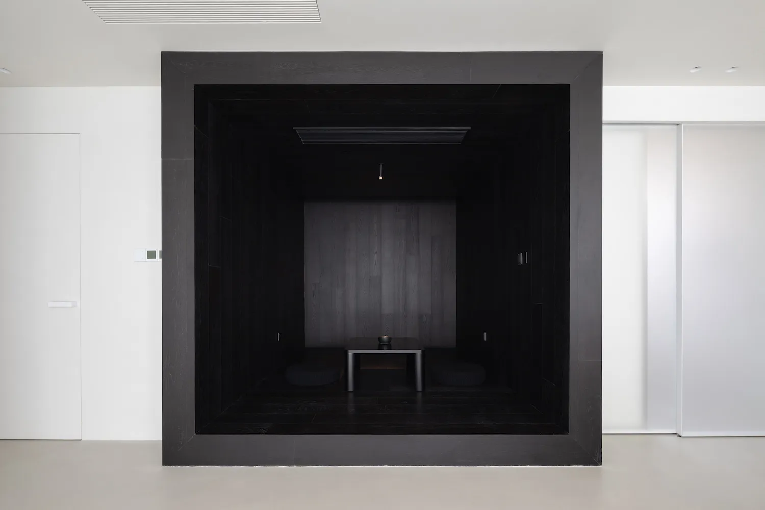 A minimalist black cube living room with wooden flooring and a small table.