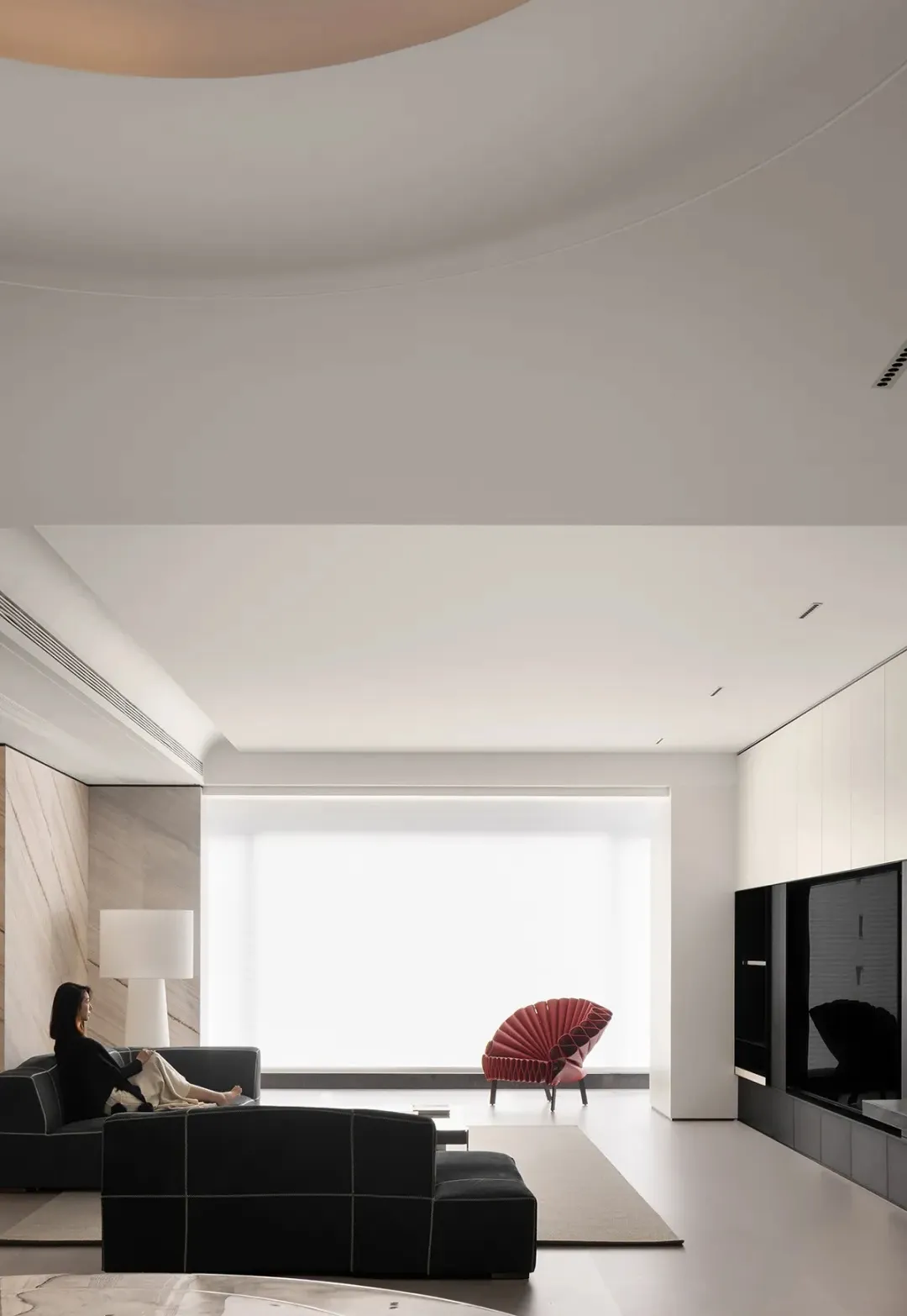 A modern living room with a black sofa, a red chair, and a large window.