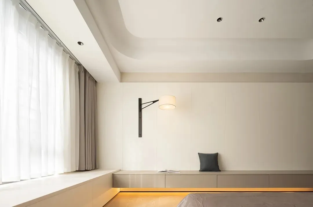 Modern minimalist bedroom with grey bed, wooden floor, and floor-to-ceiling windows.