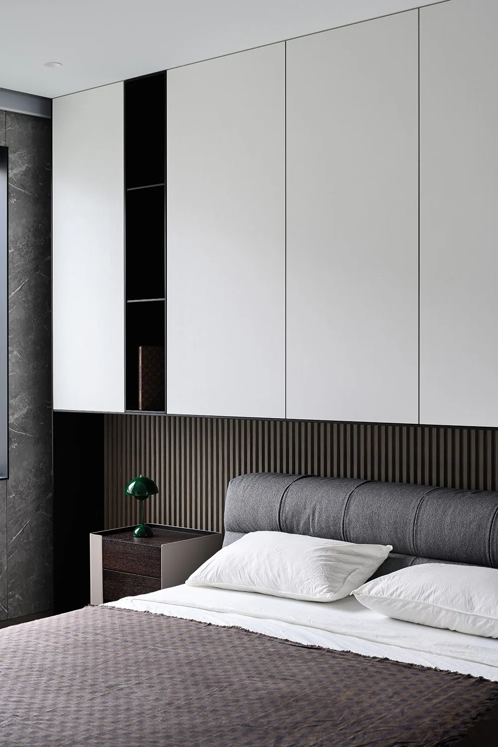 A minimalist bedroom with wooden walls and floor, featuring a bed with white linens and a speaker on a stand.
