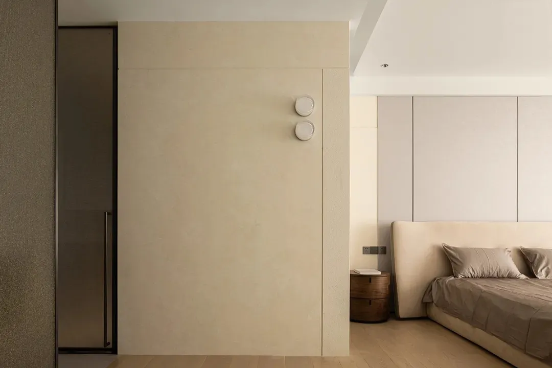 Neutral-toned minimalist bedroom featuring a large bed, side table, and minimalist wall panels.